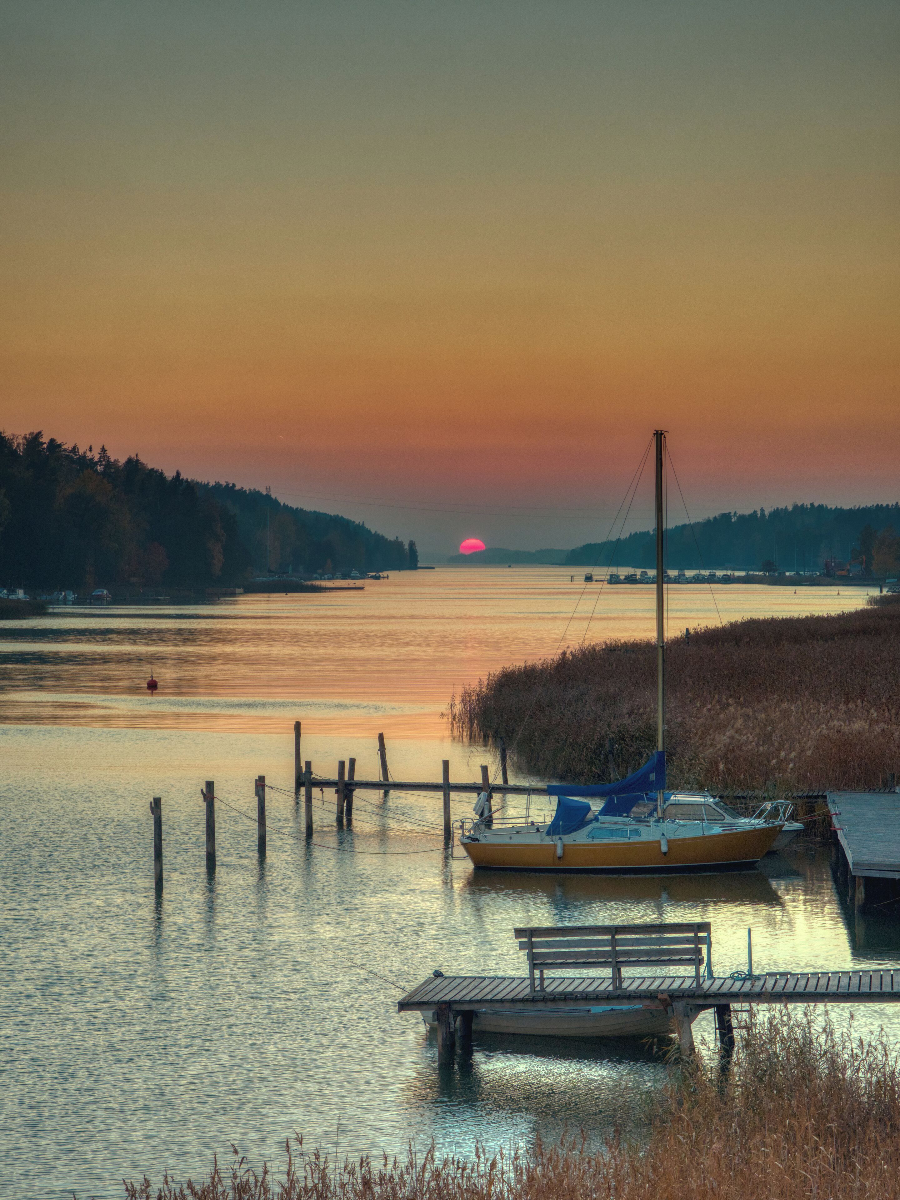 A sunset over a calm lake with a dock and a small boat.