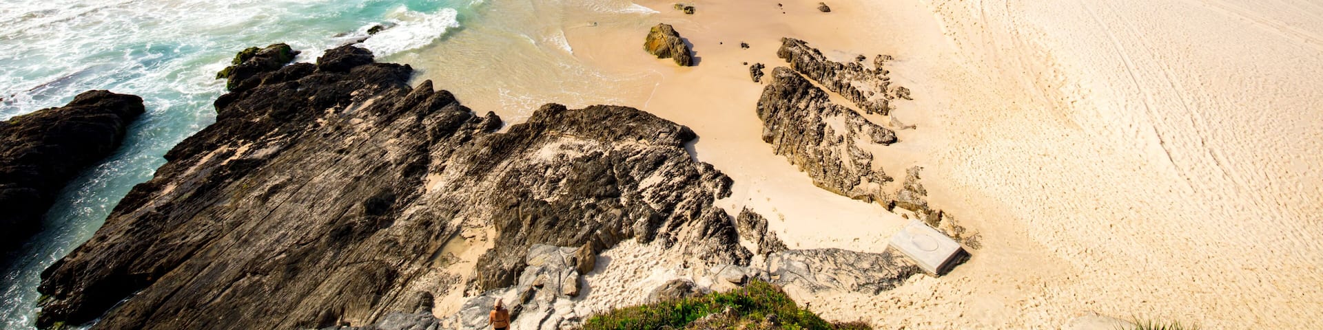 Una playa con aguas turquesas cristalinas, orilla de arena y afloramientos rocosos.