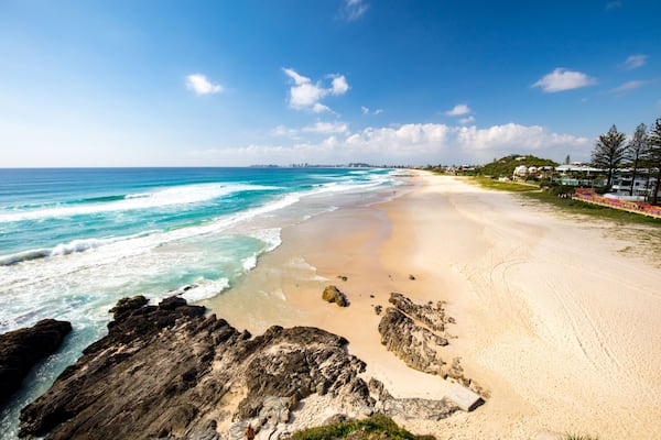 Ein Strand mit klarem türkisblauem Wasser, sandigem Ufer und Felsenformationen.