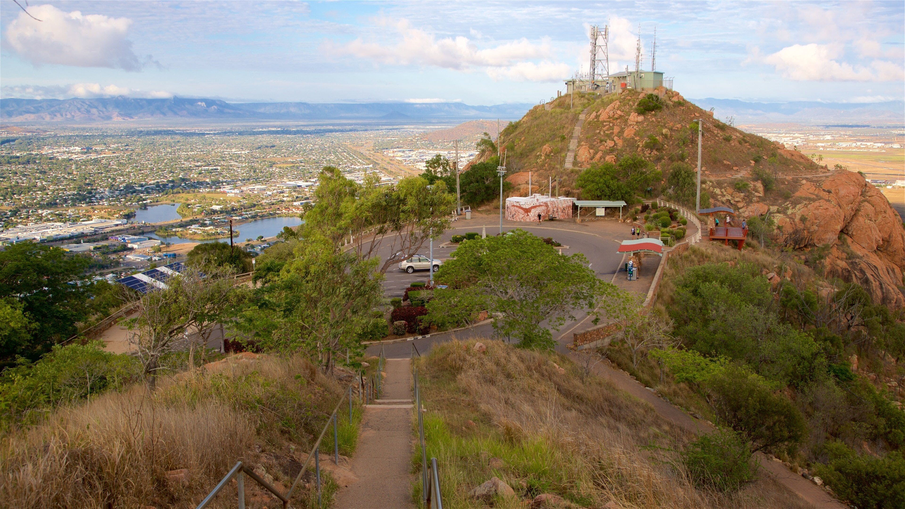 A mountainous landscape with a town at the base, a lake, and a telecommunications tower.