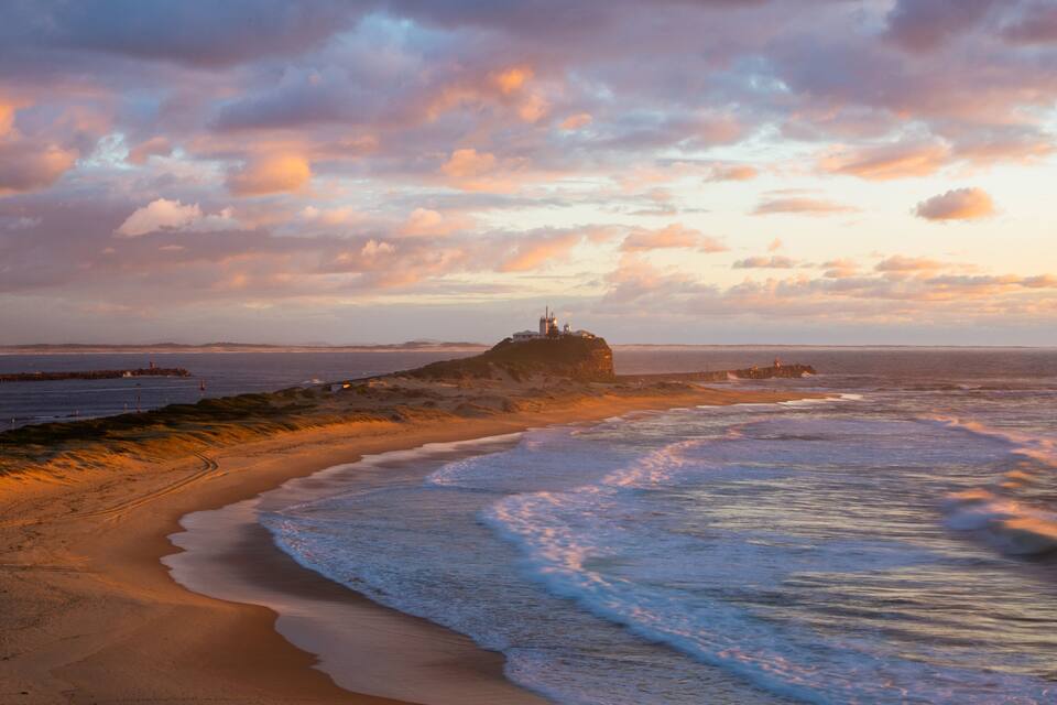 A coastal landscape with a lighthouse on a rocky outcrop, sandy beach, and ocean waves.