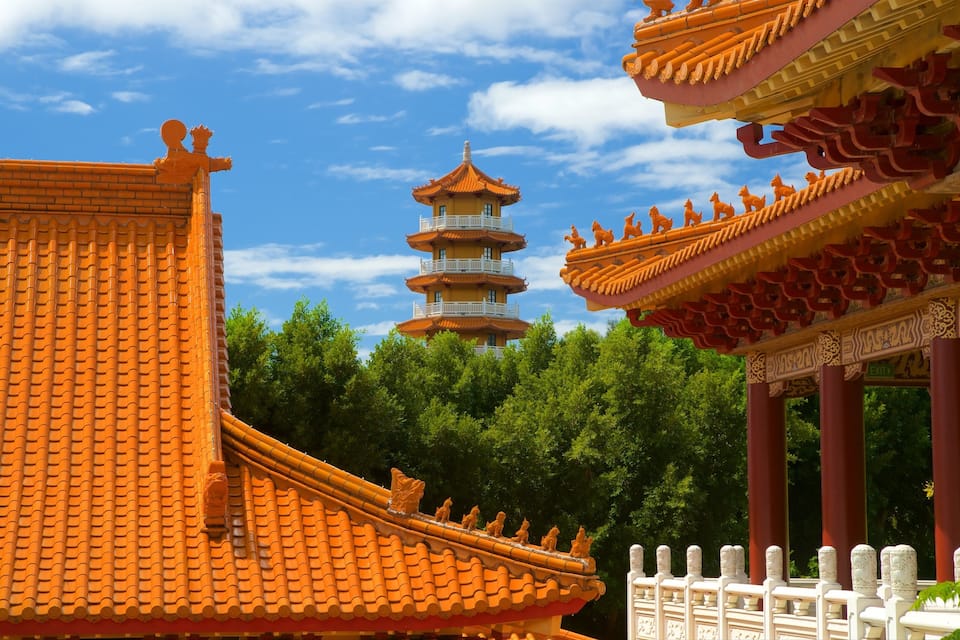 A traditional Chinese pagoda with multiple tiers, surrounded by lush green trees and orange-roofed buildings.