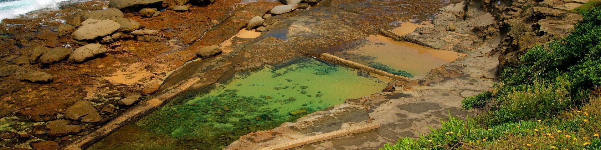 Un paysage côtier caractérisé par une rive rocheuse, des eaux d’un bleu limpide et une plage de sable.