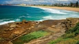 A coastal landscape with a rocky shoreline, clear blue waters, and a sandy beach.