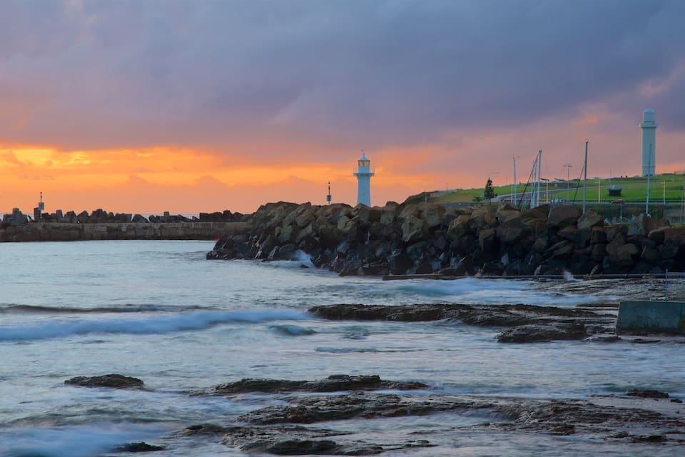 A coastal scene with lighthouses, rocky breakwaters, and a sunset.