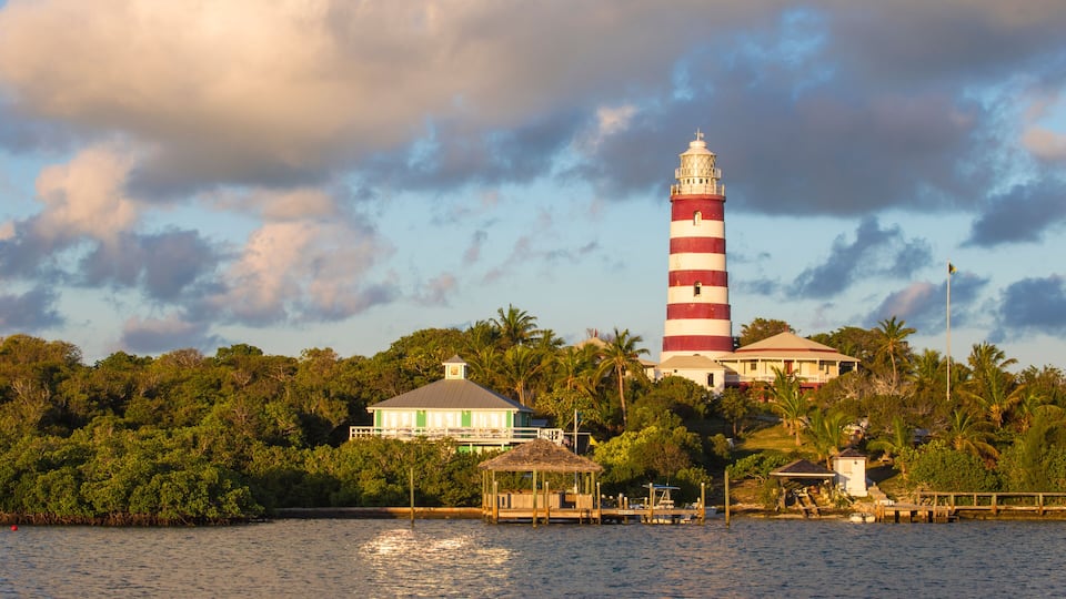 A lighthouse with red and white stripes, a white building with a green roof, and lush greenery.