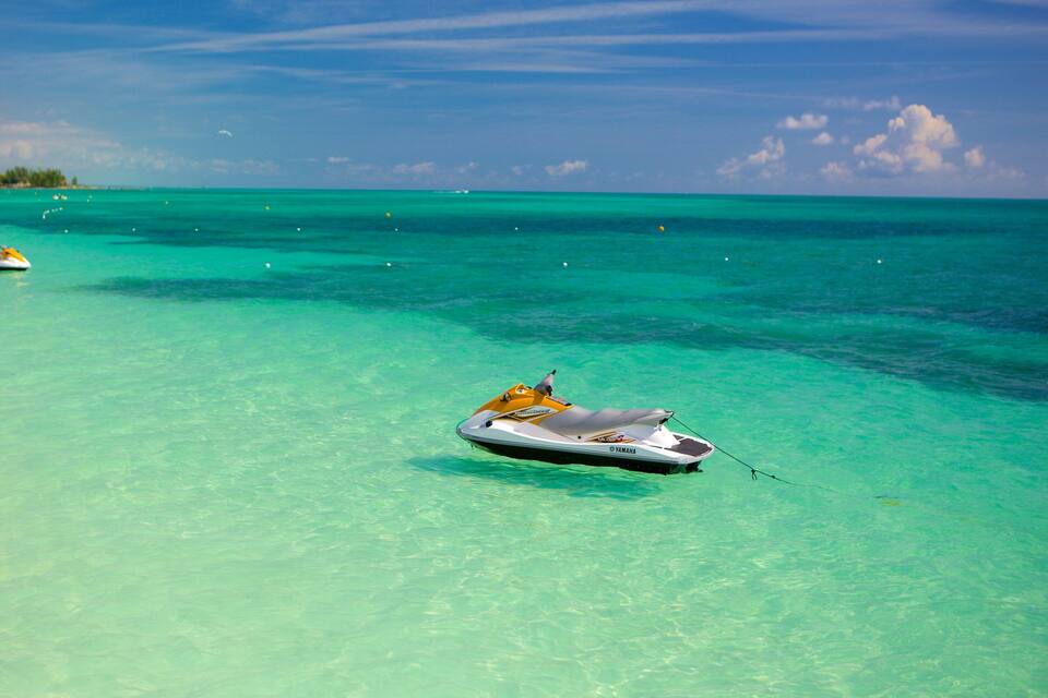 A clear turquoise sea with a jet ski in the foreground and several boats in the background.