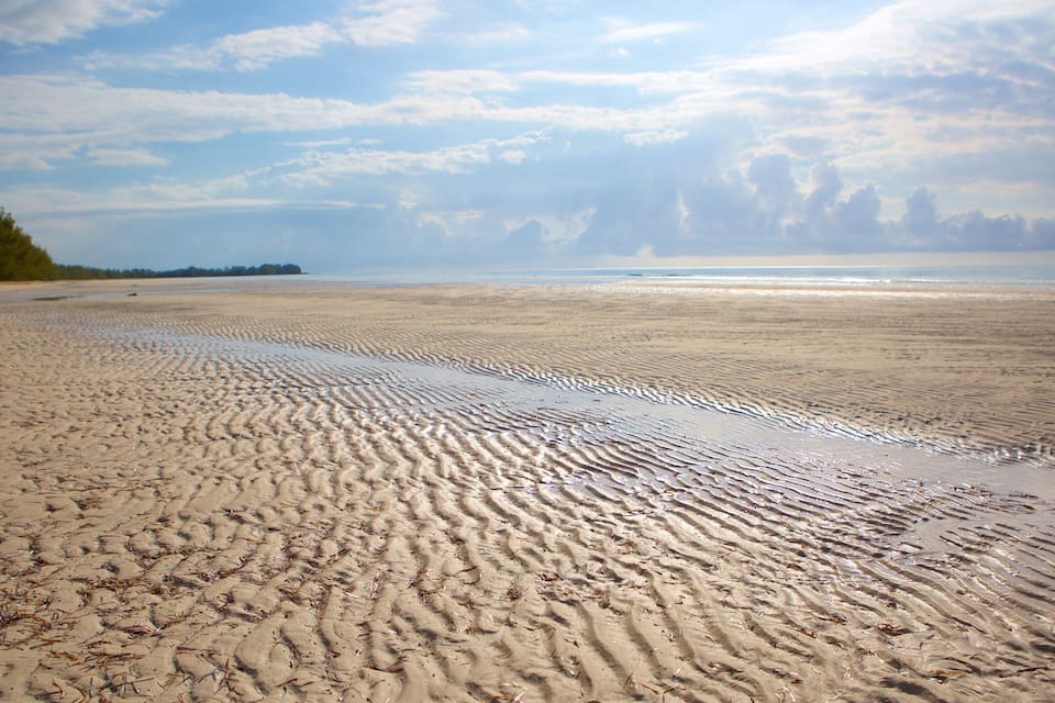 A wide sandy beach with gentle waves and a distant shoreline.