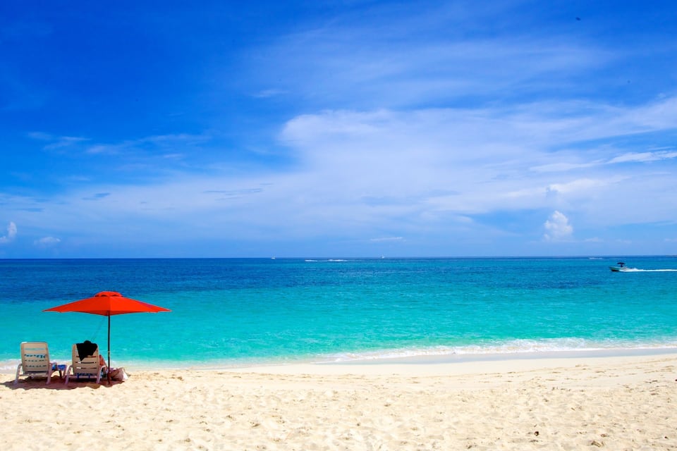 Une plage avec deux chaises longues et un parasol rouge, une eau turquoise et un ciel dégagé.
