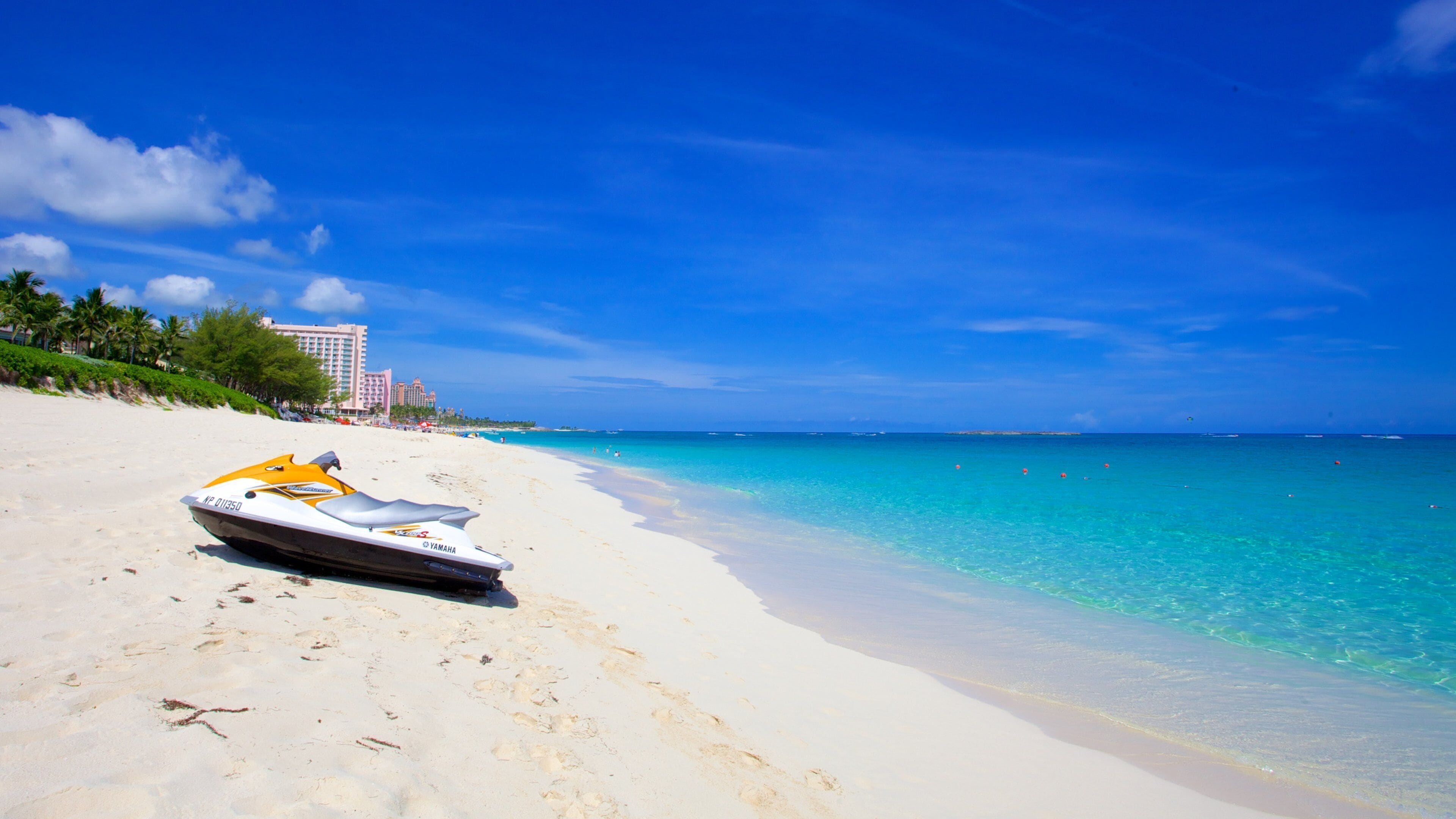 A beach with a jet ski, clear turquoise water, and a hotel in the background.