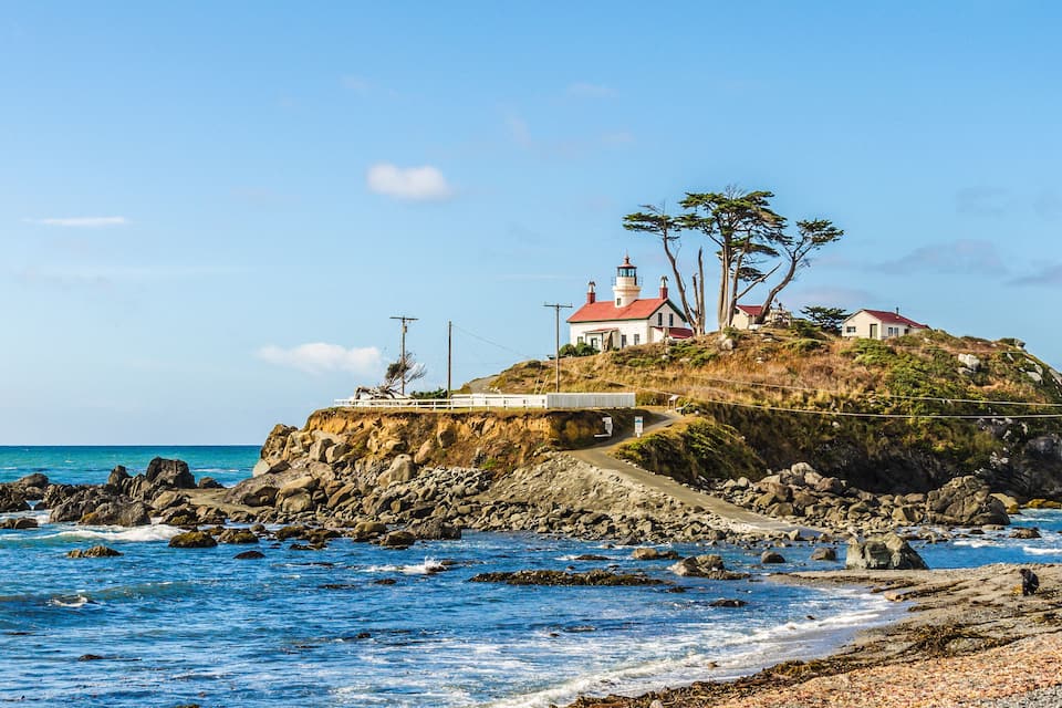 A coastal lighthouse on a rocky outcrop with a clear blue sky.