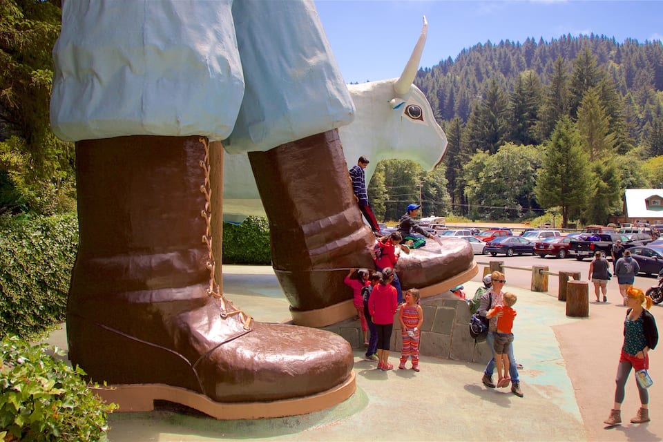 A large sculpture of a giant shoe with a unicorn's head, surrounded by people and parked cars.