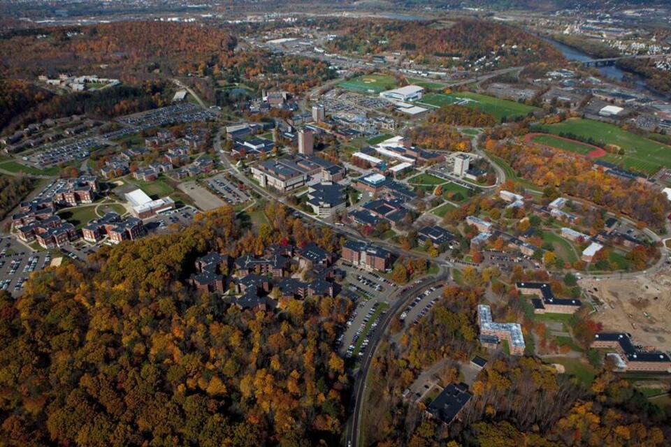 An aerial view of a campus with buildings, parking lots, and autumn-colored trees.