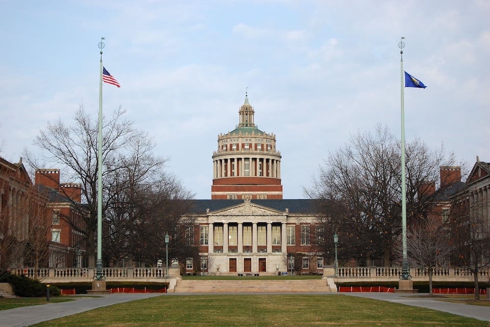 A large building with a central dome and two flagpoles with flags.