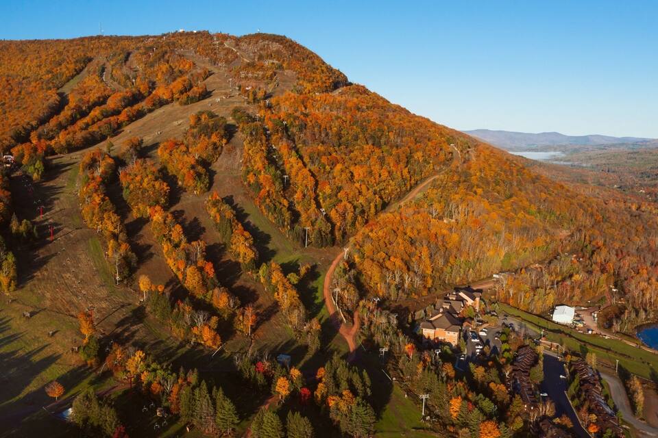 A mountainous landscape with autumn foliage, a ski lift, and a lake.
