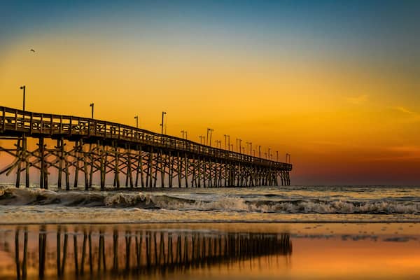 A pier extending into the ocean with waves crashing against it during sunset.