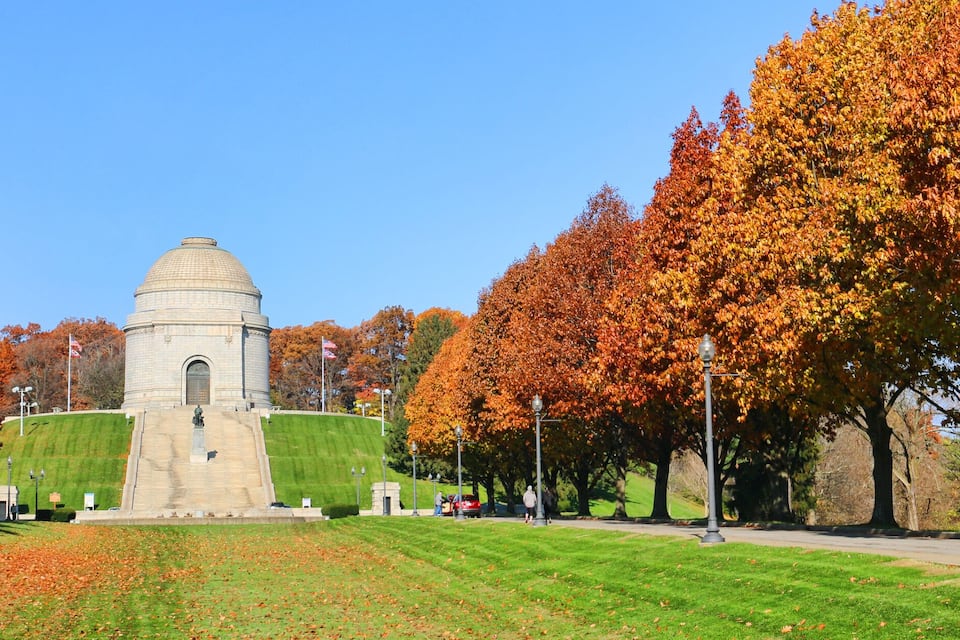 A park with a large dome building, surrounded by trees with autumn foliage.