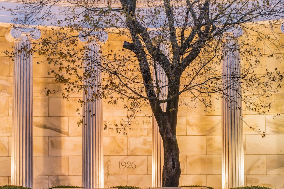 A tree in front of a building with columns and a plaque.