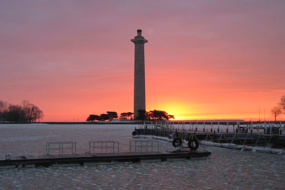Un monumento alto al atardecer, una masa de agua congelada y un muelle con barandillas.