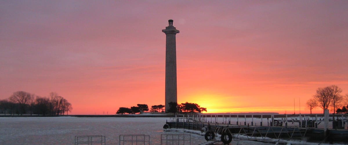 A tall monument at sunset, a frozen body of water, and a pier with railings.
