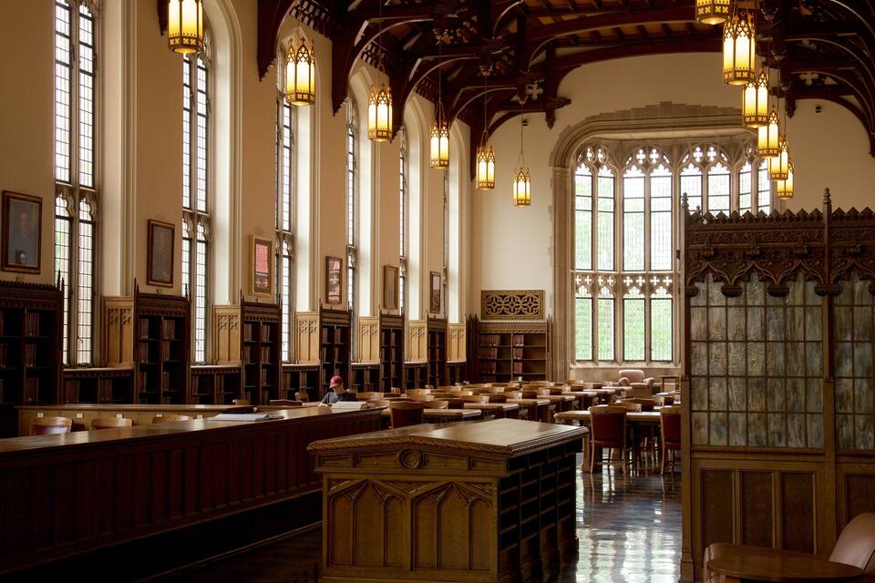 Una biblioteca con ventanas altas, estanterías de madera y candelabros ornamentados.