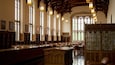 Una biblioteca con ventanas altas, estanterías de madera y candelabros ornamentados.