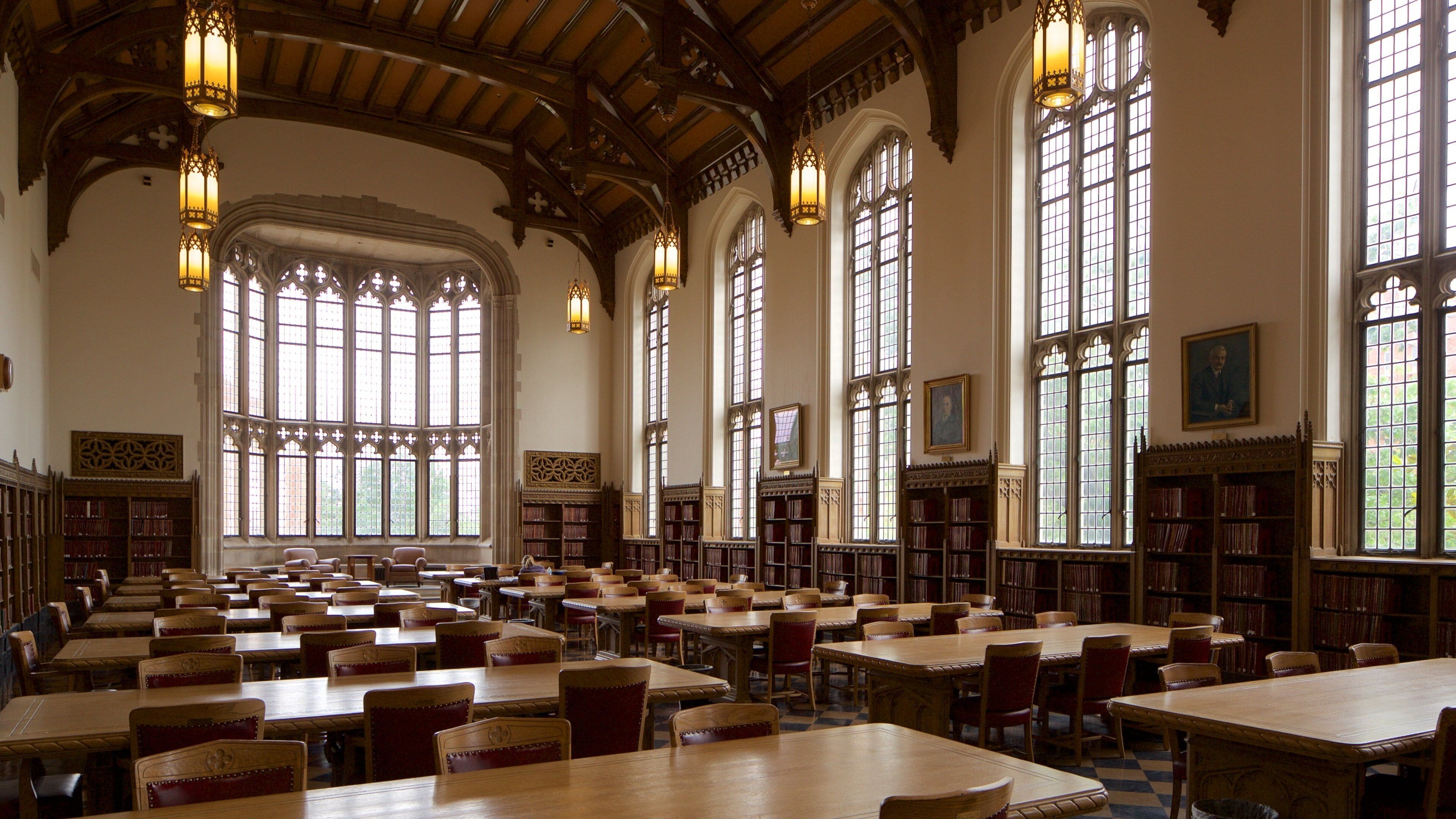 A large library with high wooden ceilings, tall windows, and rows of bookshelves.