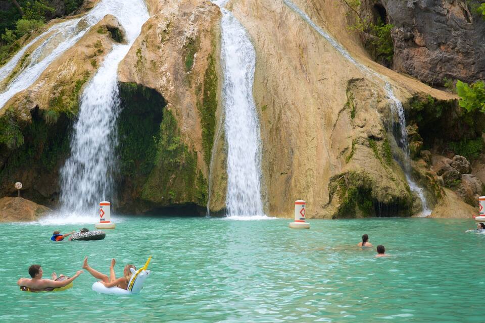 Una cascata con persone che nuotano e galleggiano nell'acqua.