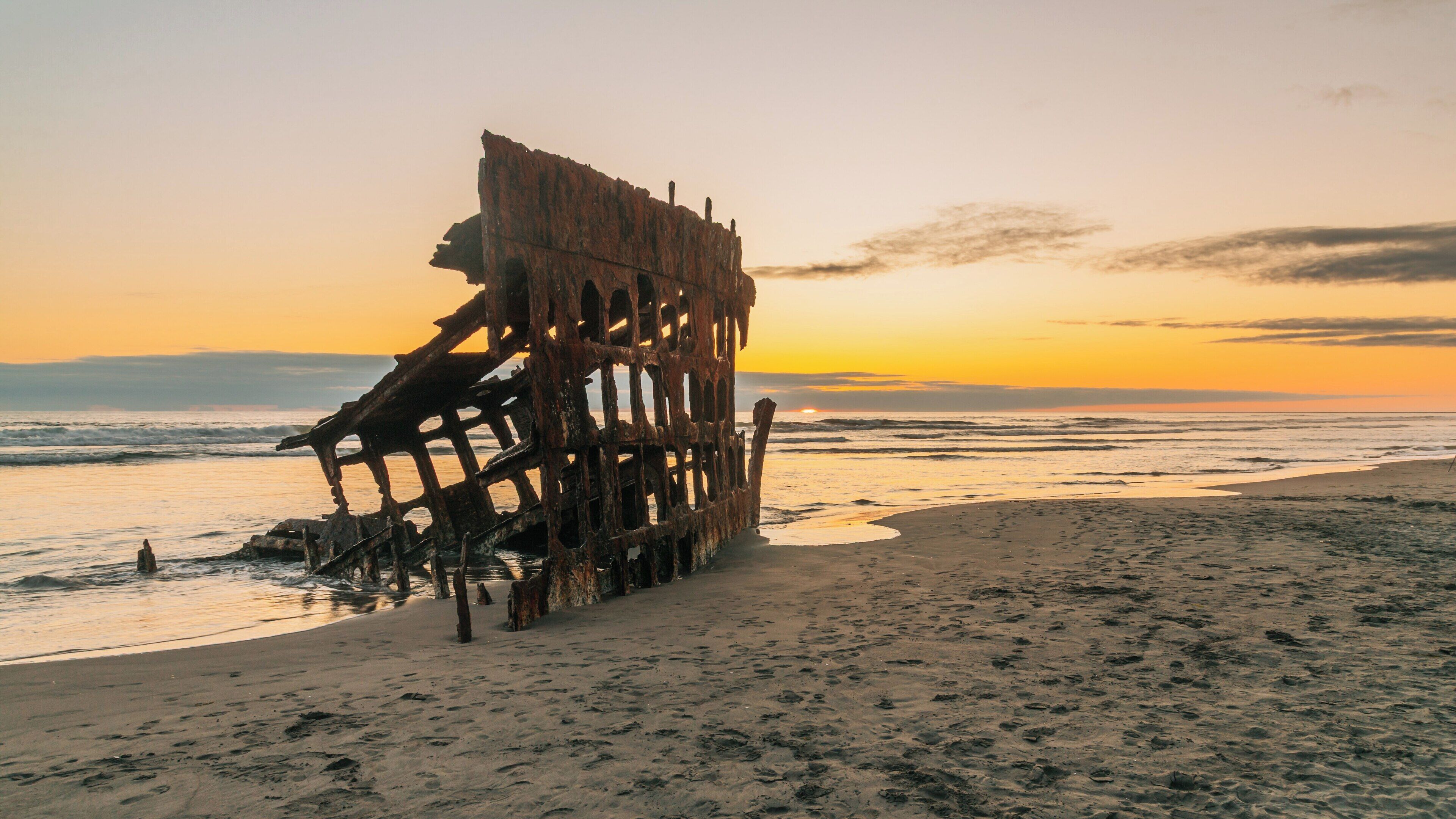 Rusty shipwreck under a vibrant sunset at Fort Stevens State Park in Astoria, Oregon, showcasing nature's beauty and history by the ocean shoreline