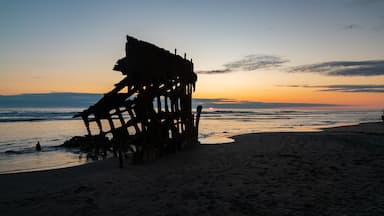 A beach with a large, rusted metal structure silhouetted against a sunset.
