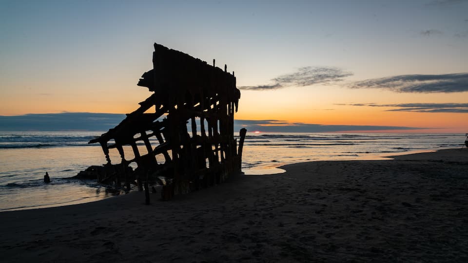 A beach with a large, rusted metal structure silhouetted against a sunset.