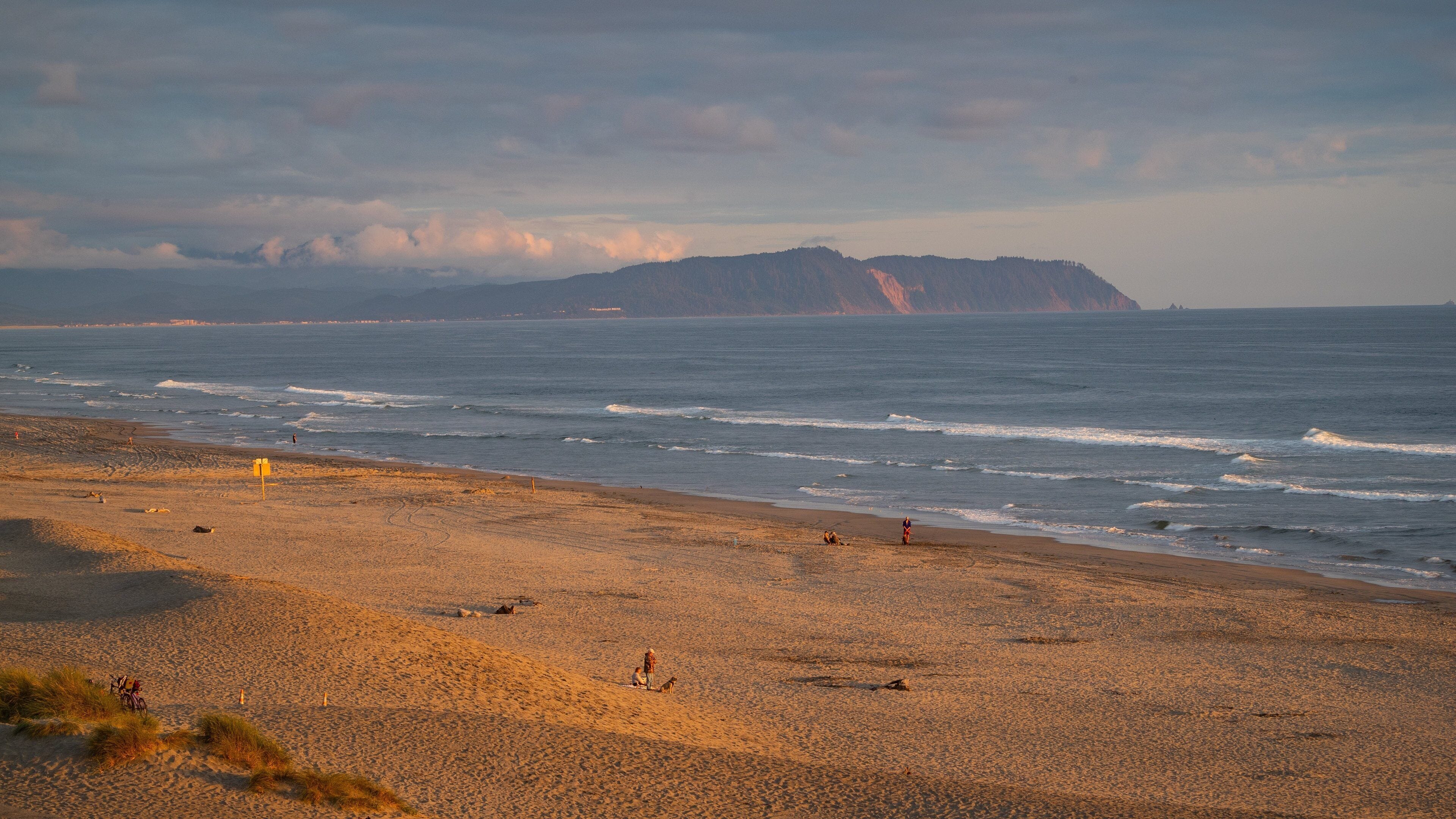 A beach with waves, a distant mountain, and a cloudy sky.