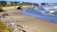 Una playa arenosa con rocas grandes, olas y una costa rocosa distante.
