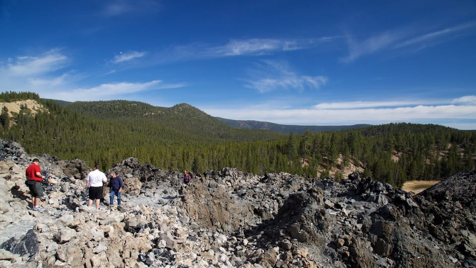 A rocky terrain with hikers and a forested mountain range in the background.