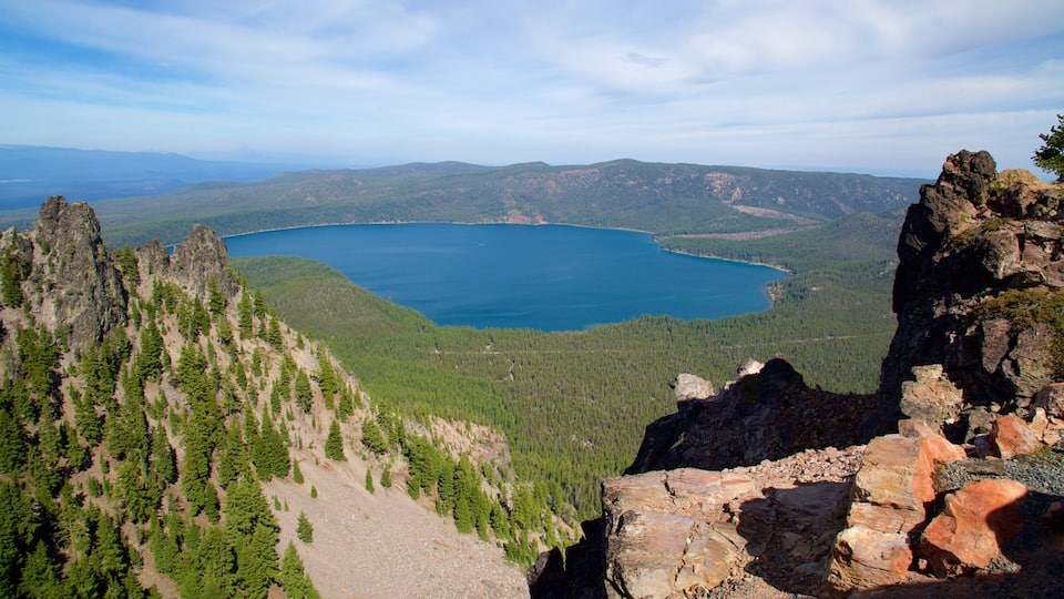 A mountainous landscape with a lake surrounded by dense forests and rocky outcrops.