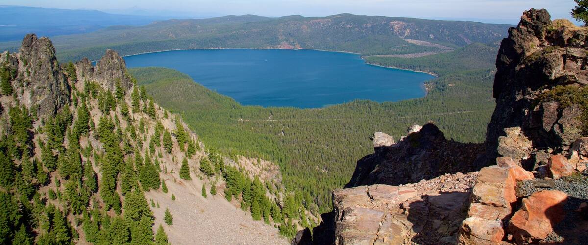 A mountainous landscape with a lake surrounded by dense forests and rocky outcrops.