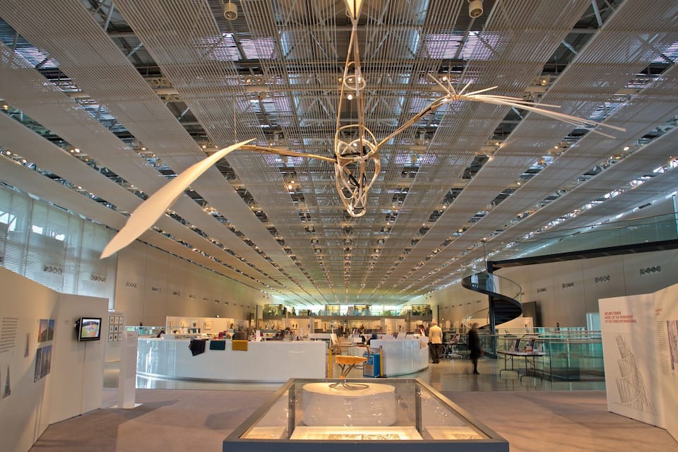 Un espacio de exhibición interior con un diseño moderno de techo, barandillas de vidrio y paneles informativos.