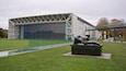 A modern building with a glass facade and a sculpture of a reclining figure in a park.