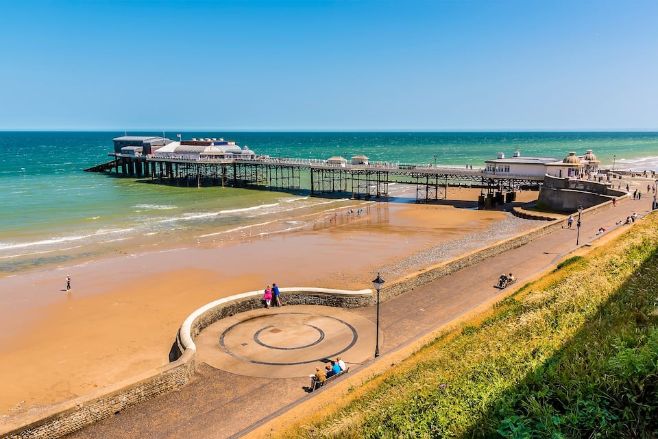 Une jetée qui s’avance dans l’océan, une plage de sable et une structure circulaire en pierre.