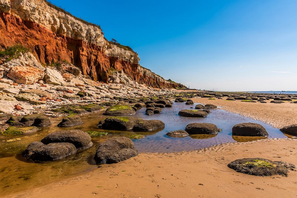 A rocky beach with large boulders and a cliff with red and white layers.