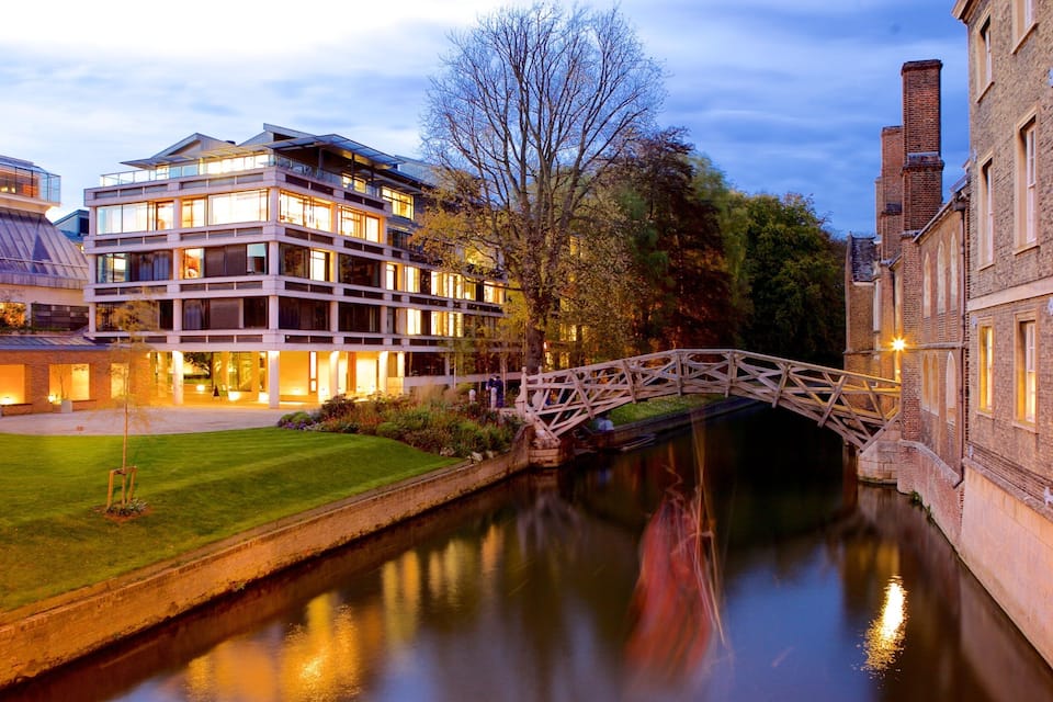 A modern building with a glass facade, a wooden bridge over a canal, and traditional brick buildings.