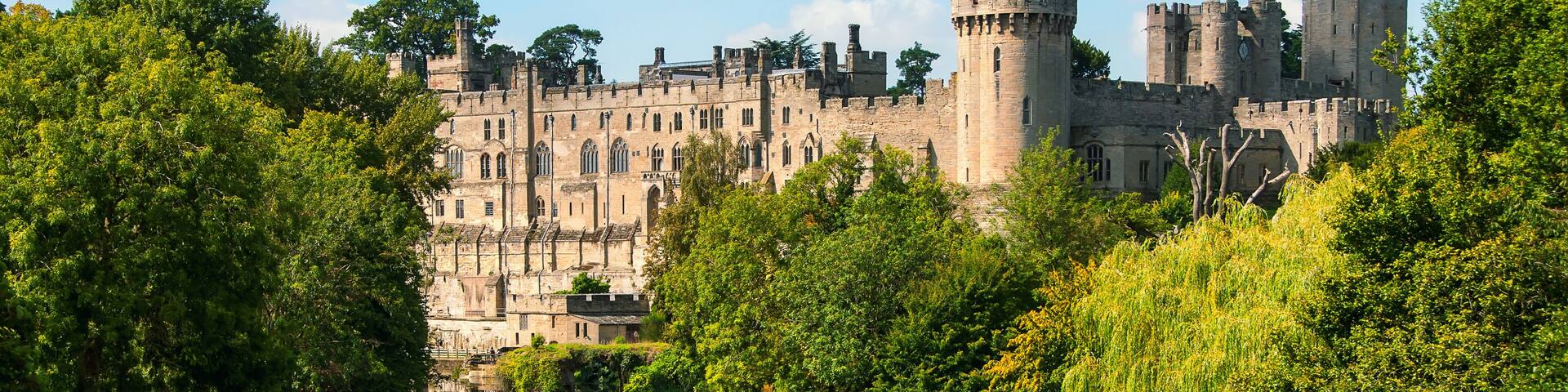A castle with a river in the foreground and lush greenery.