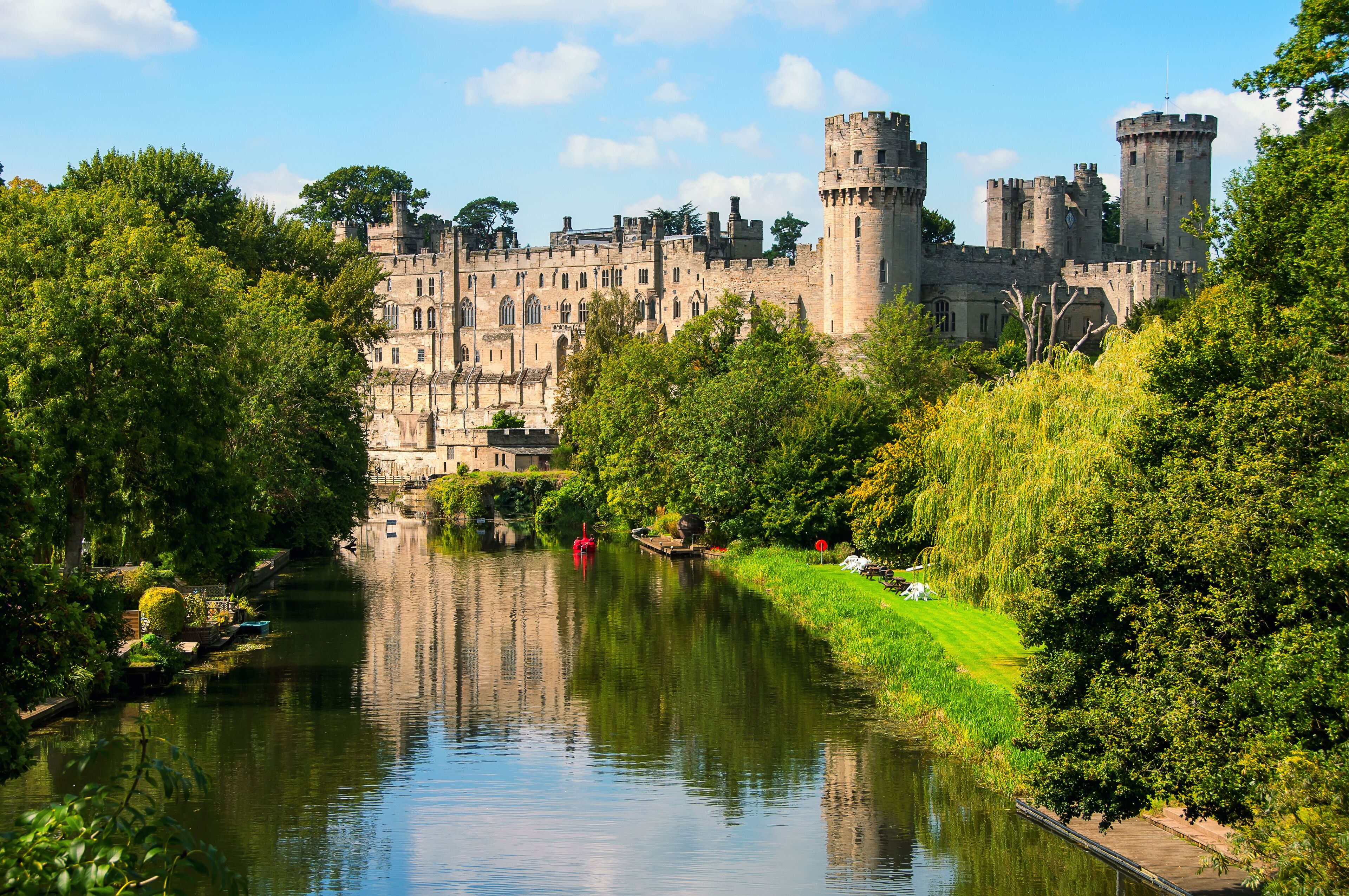 A castle with a river in the foreground and lush greenery.
