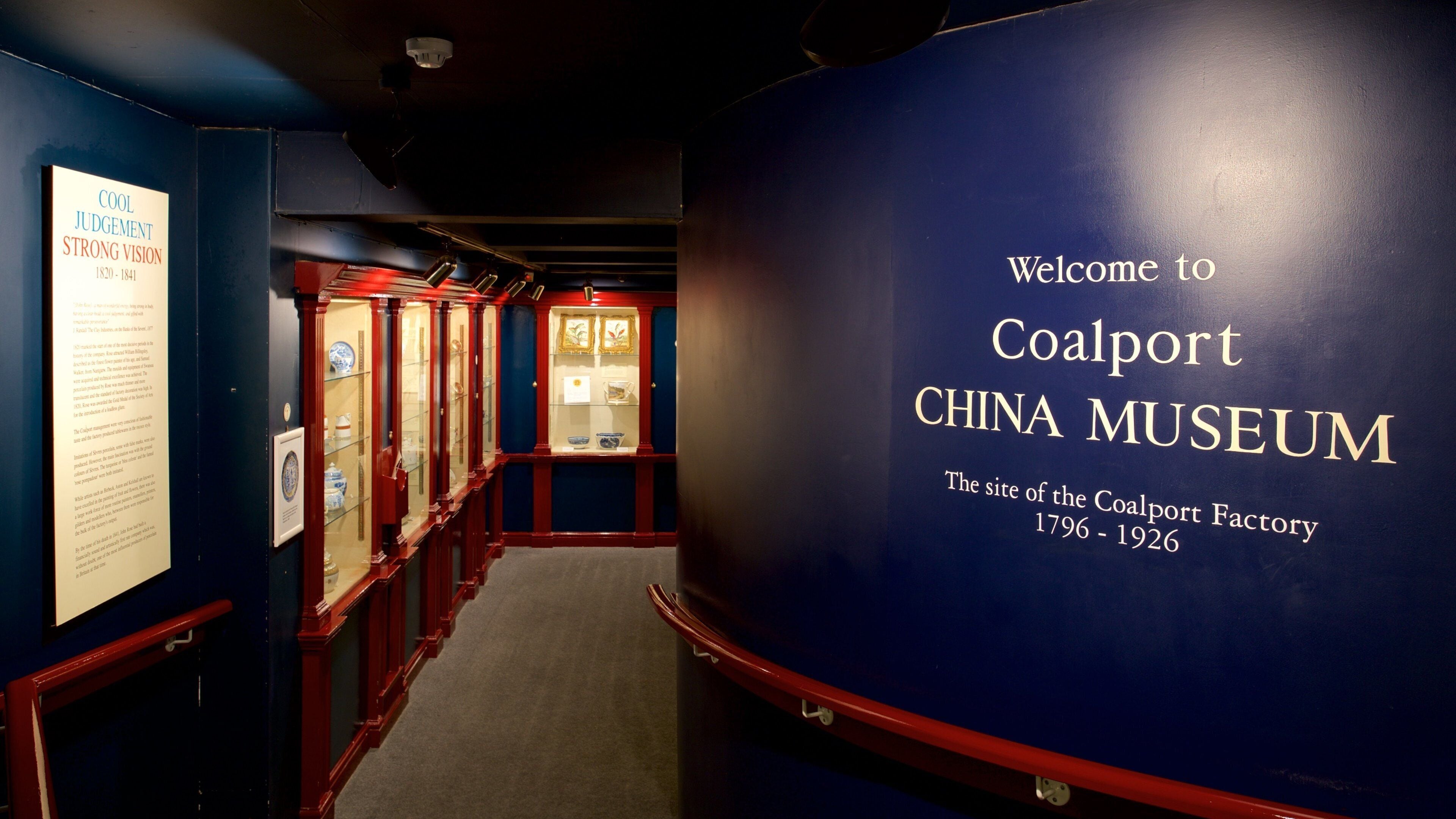 A corridor with display cases and a large blue wall with the text "Welcome to Coalport China Museum".
