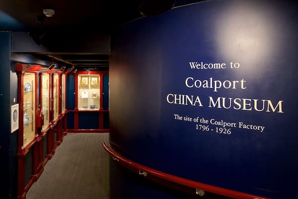 Un couloir bordé de vitrines et un grand mur bleu sur lequel est inscrit le texte : « Bienvenue au musée de la porcelaine de Coalport ».