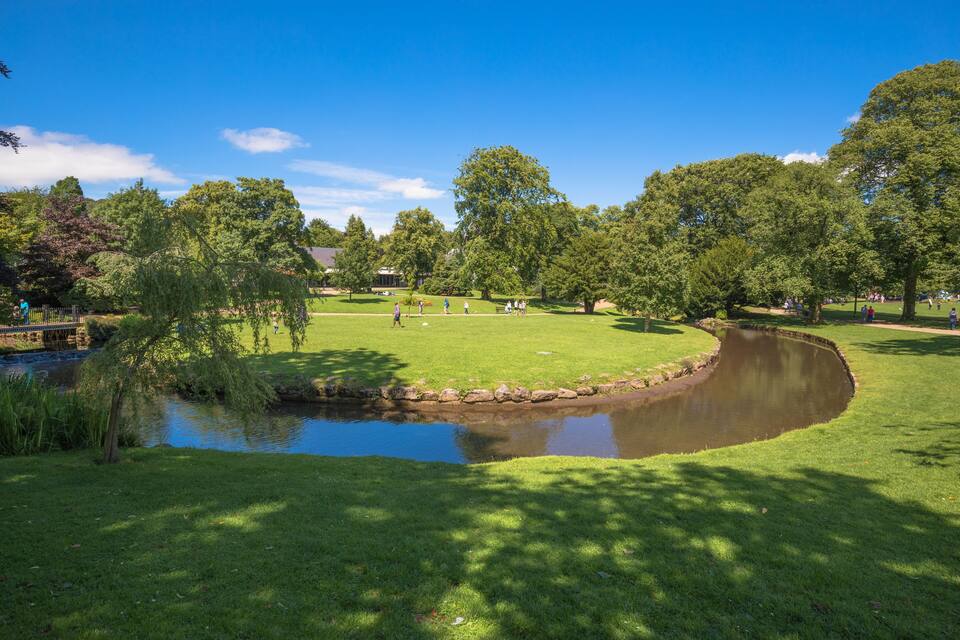 A park with a pond, green grass, trees, and a bridge.