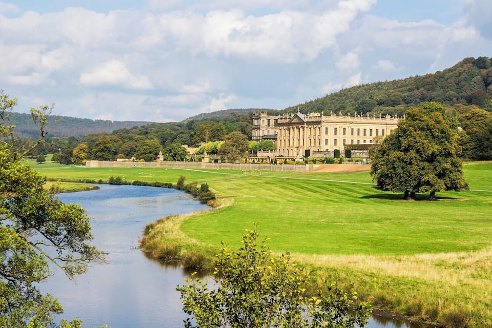 A large stately building with a formal garden and a river in the foreground.