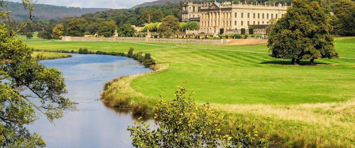 A large stately building with a formal garden and a river in the foreground.