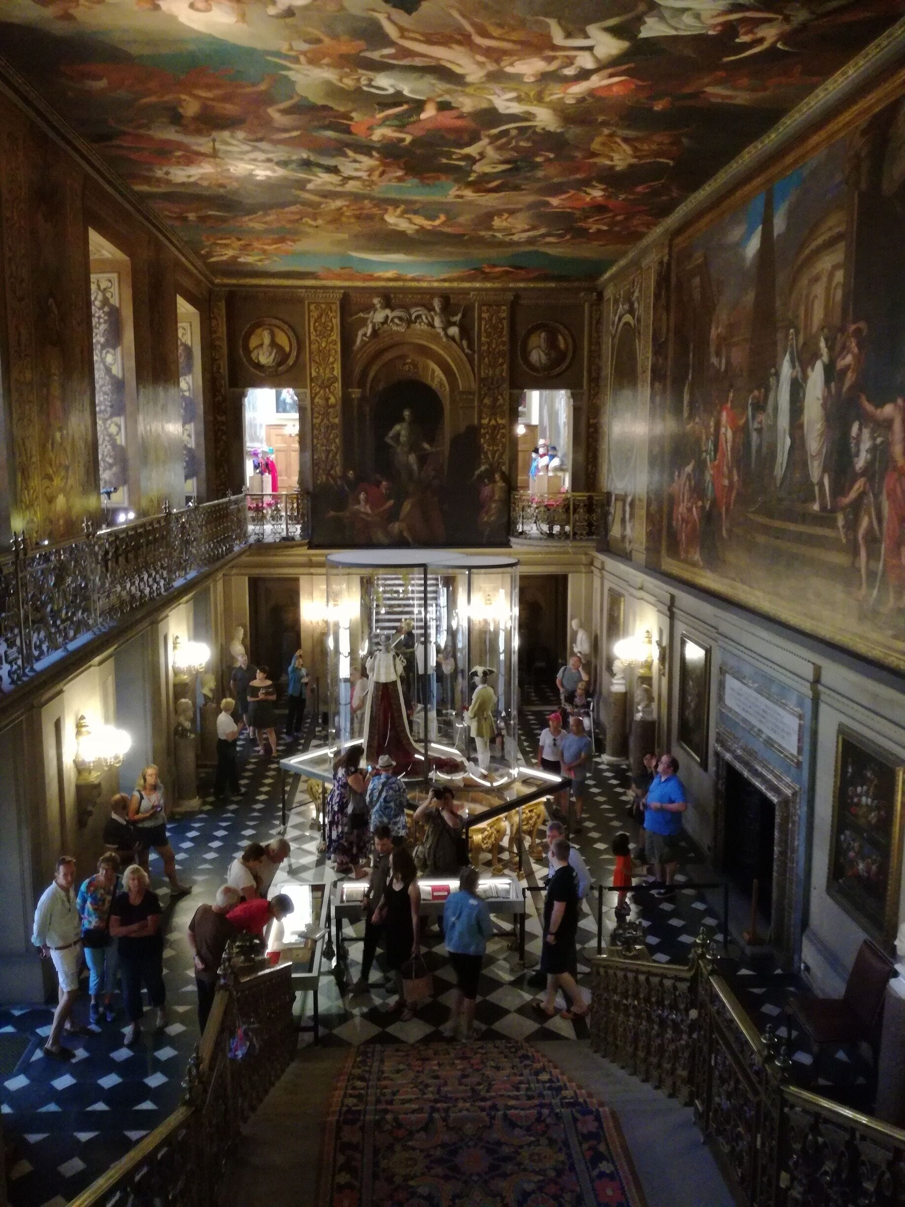 Un salón majestuoso con techos ornamentados, una escalera central y pinturas clásicas.