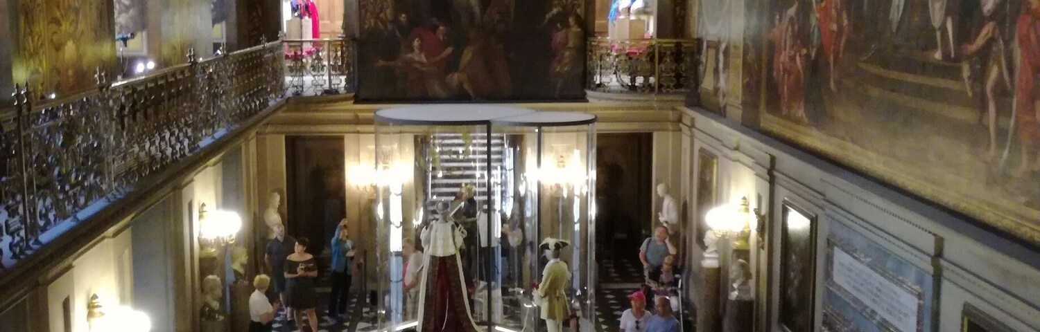 Un salón majestuoso con techos ornamentados, una escalera central y pinturas clásicas.